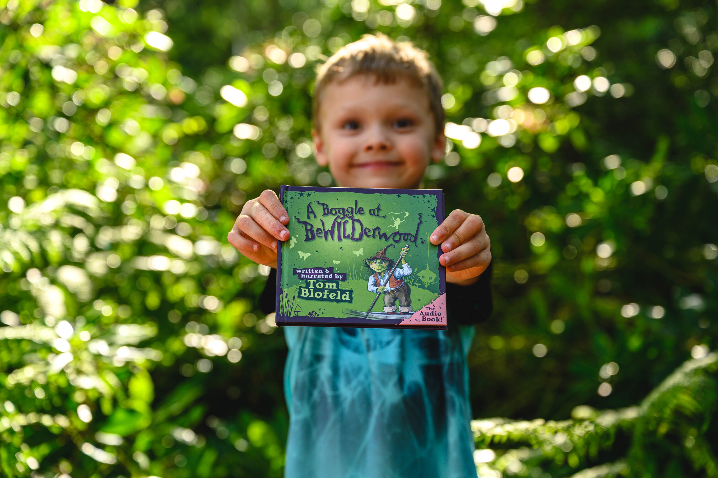 A child holds a copy of "A Boggle at BeWILDerwood: The Audiobook"