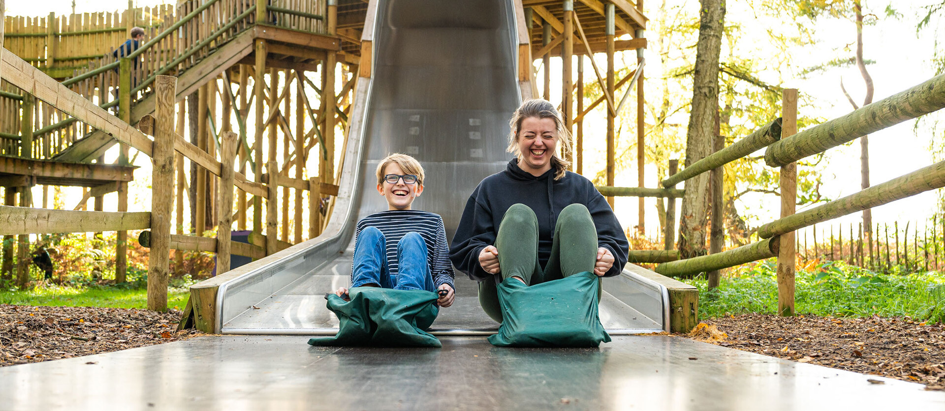 A mother and son play on a wide slide at BeWILDerwood