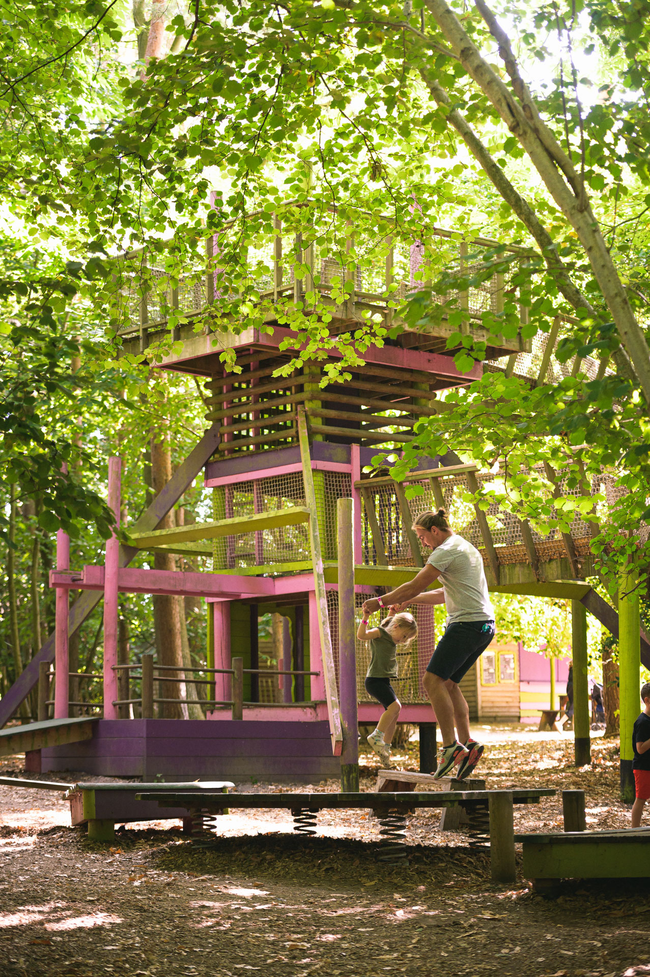 Dad and daughter jumping on a wooden structure at Bewilderwood