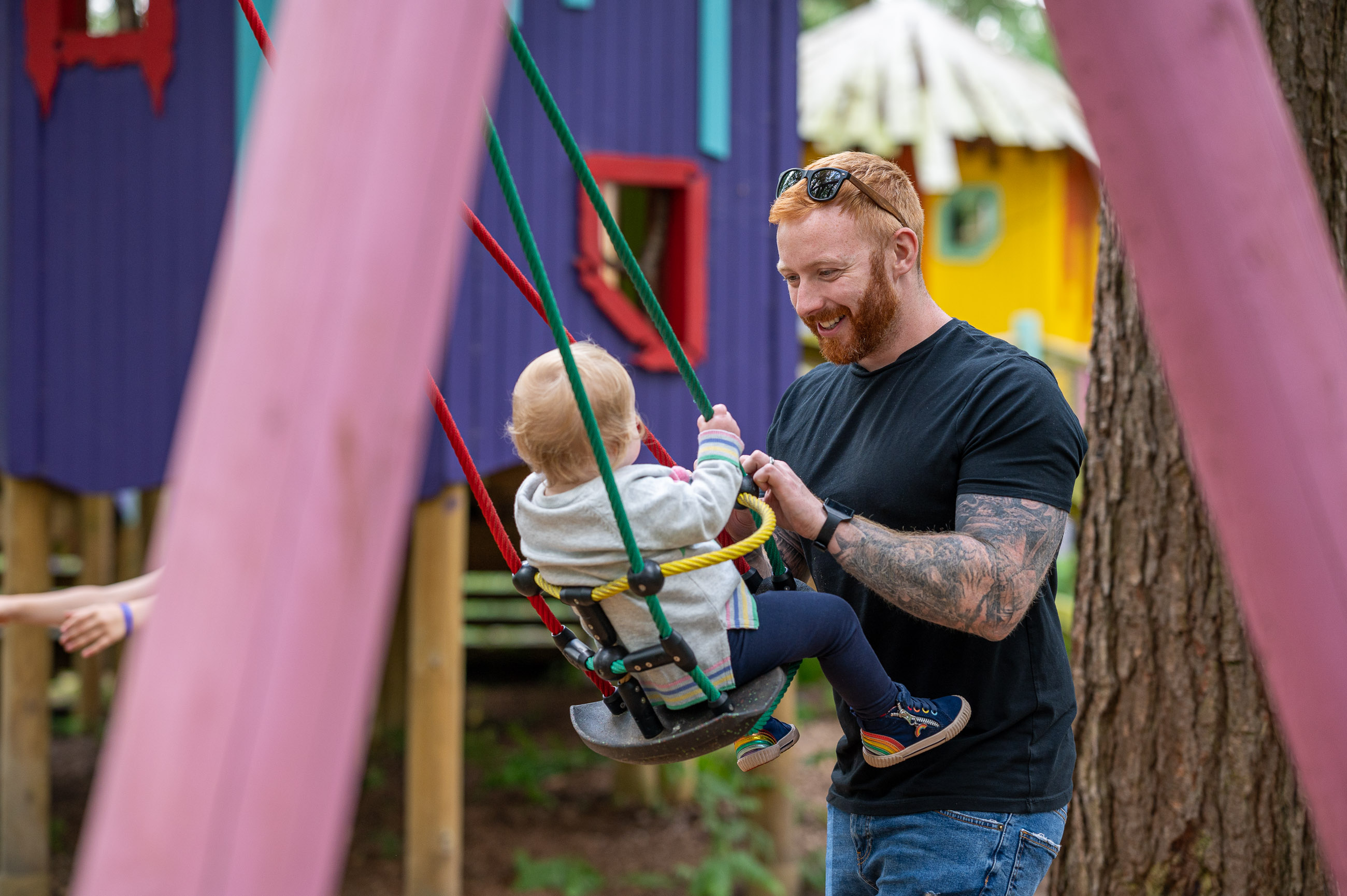 Father pushing child on swing with colourful houses behind them at bewilderwood