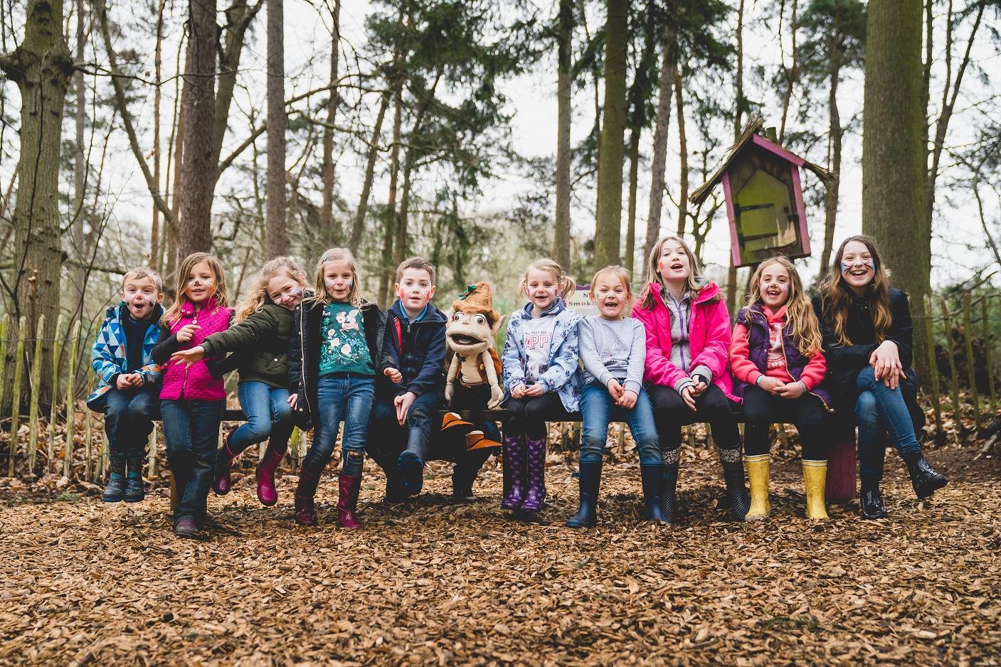 A group of school children and Swampy are sat on a bench in autumn 