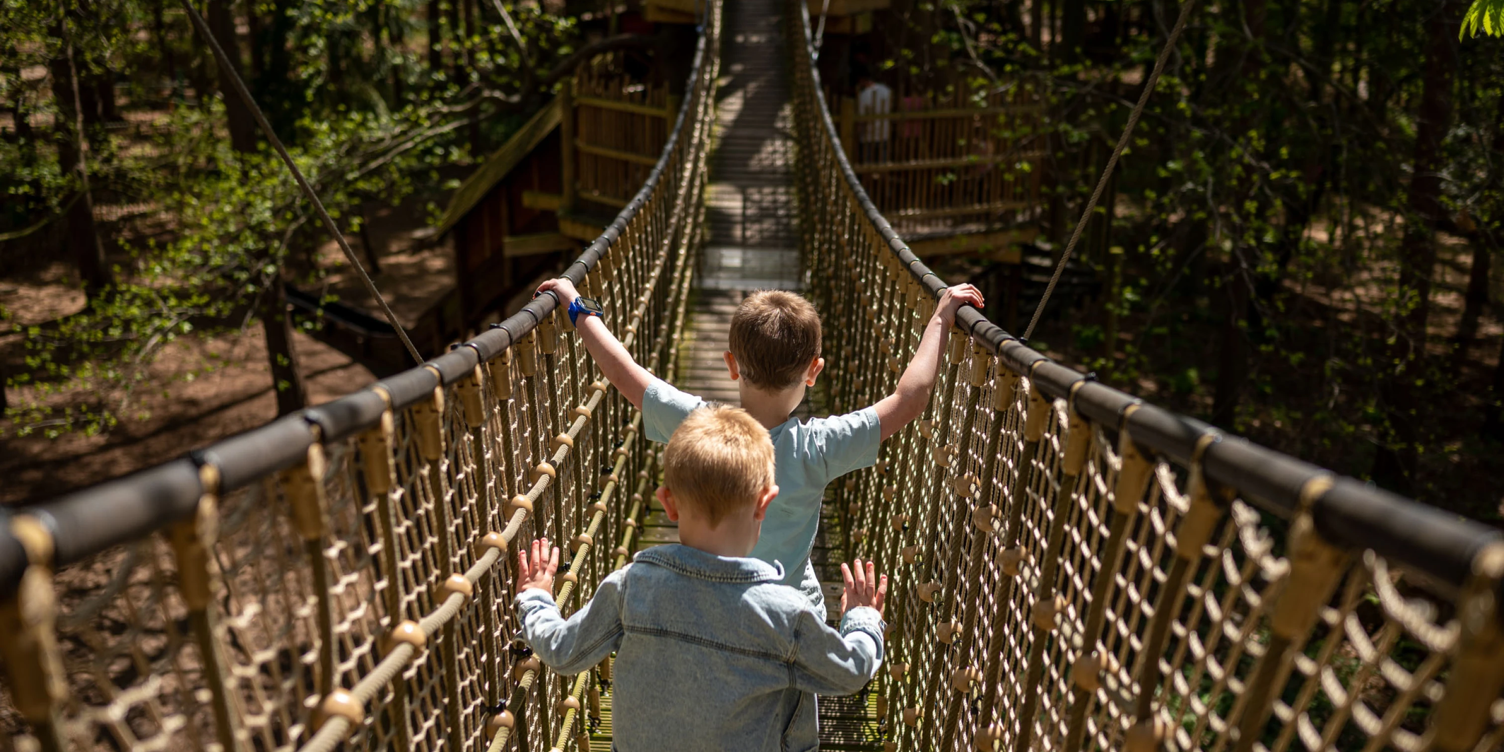 2 boys walking along a high up bridge at Bewilderwood